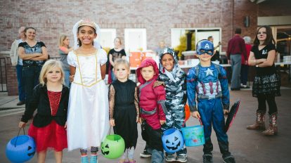 children standing while holding Jack 'o lantern and wearing costume