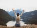 woman sitting on cliff raising both hands