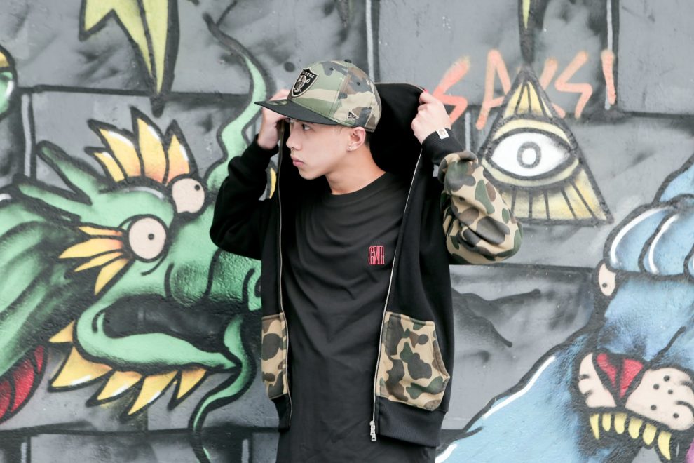 man in black and white adidas hoodie standing beside wall with graffiti