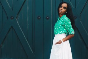 woman in white skirt and green dress shirt hand on pocket standing at the front of green door