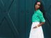 woman in white skirt and green dress shirt hand on pocket standing at the front of green door