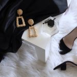 pair of gold-colored earrings on table and black ankle-strap pumps on area rug