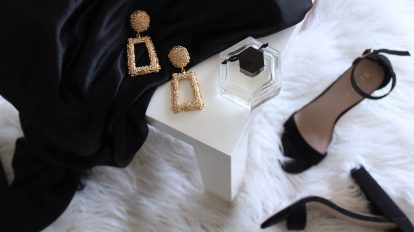 pair of gold-colored earrings on table and black ankle-strap pumps on area rug