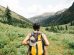 person carrying yellow and black backpack walking between green plants