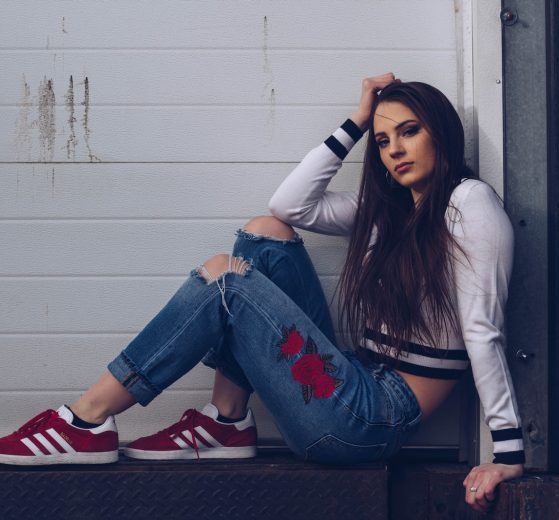 woman in white long sleeve shirt and blue denim jeans sitting on white wooden fence